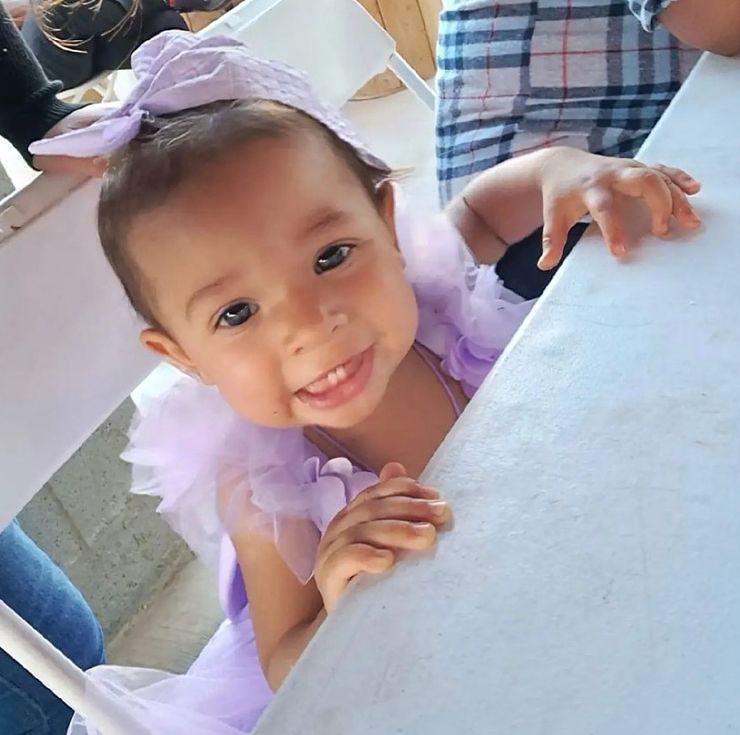 Amalia, a toddler, smiling in a lavender dress with a matching headband