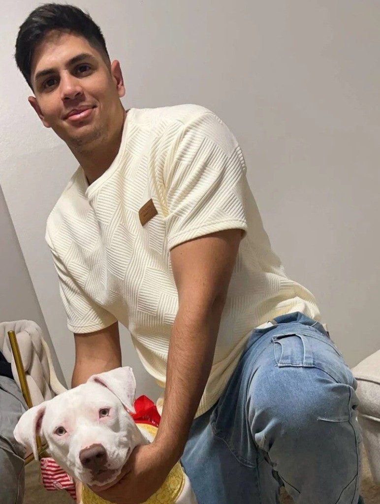 Frengel Reyes Mota kneeling indoors with a white dog, wearing a textured cream t-shirt and light-wash jeans